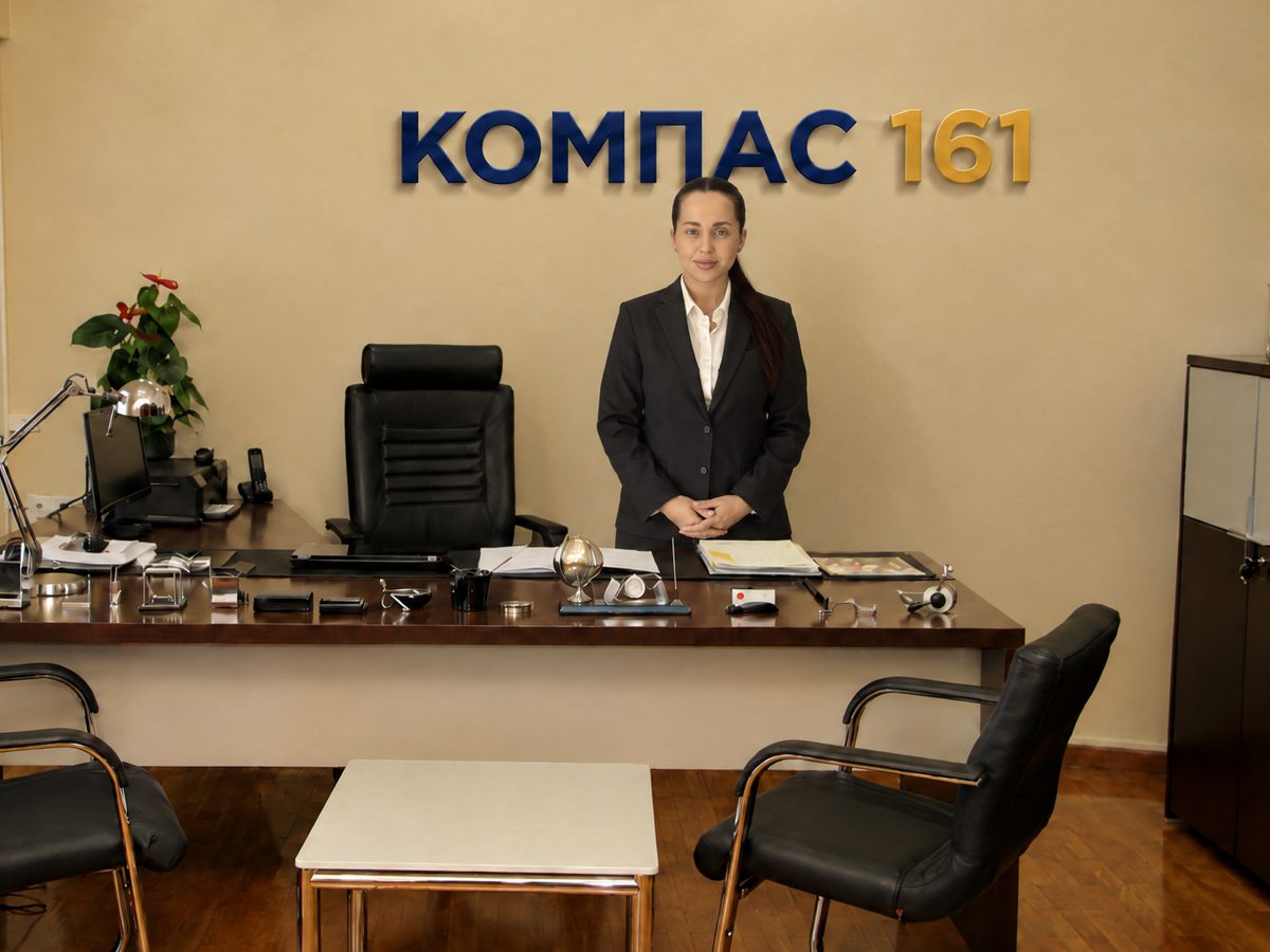 Анастасия Михайленко, главный юрист «Компас 161», в кабинете у стола, на стене надпись «Компас 161»